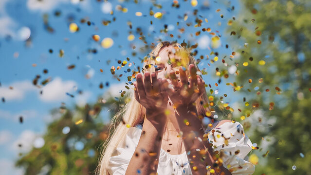 The girl blows a golden confetti out of her hands.
