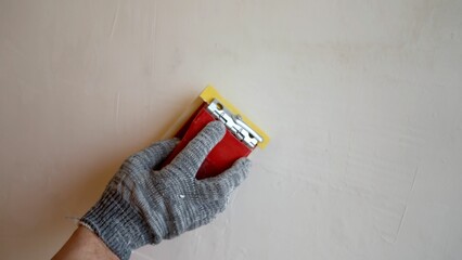 Peeling off uneven surfaces on a putty wall, sanding the freshly plastered wall surface with...