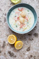 Green bowl with scallop chowder on a light-brown granite background, vertical shot, view from above