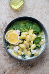 Potato gnocchi with spinach and feta served in a grey bowl, vertical shot on a beige granite...