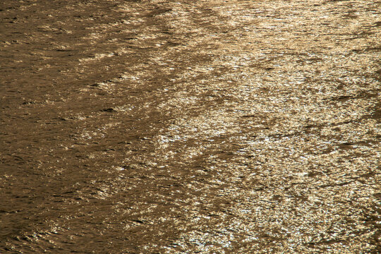 Brillo dorado sobre las olas de la superficie del agua. Reflejo de la luz del sol al atardecer sobre las aguas del río Guadiana en Sanlucar de Guadiana, Huelva, España.
