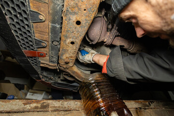 A mechanic repairs a car in a garage in a pit. A man replaces motor oil and filter in a car in the...