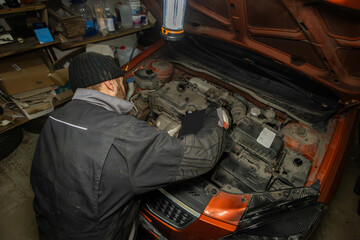 Top view of a driver pouring oil into the engine under the hood of a car in his garage. A man holds a canister of oil in his hands and carefully pours it into the engine of a car in a garage.