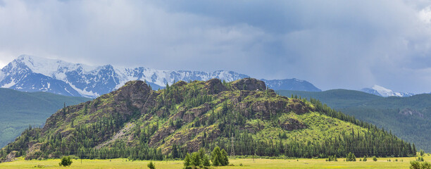 peaks in snow behind green mountains under rain