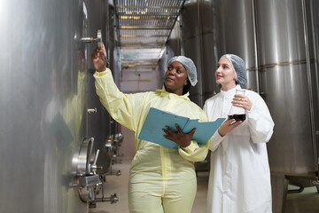 Two female winemaker inspecting quality of stainless tank during process of fermentation during...