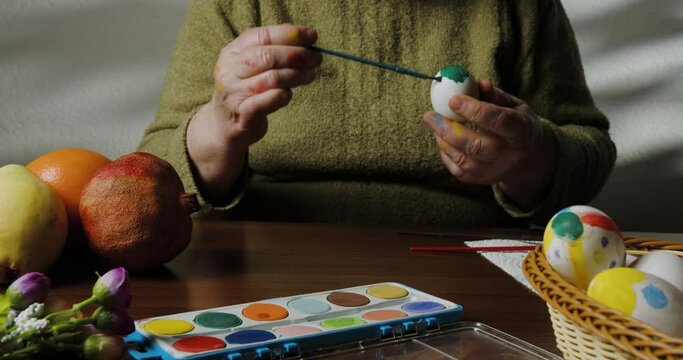  hands of a woman as she paints Easter eggs, highlighting the intricate artistry and joy of the season in a captivating close-up shot.