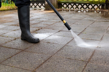 person is using a pressure washer to clean a brick patio