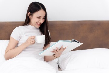 A woman comfortably relaxes in bed with a book and a coffee cup, suggesting a leisurely morning or...