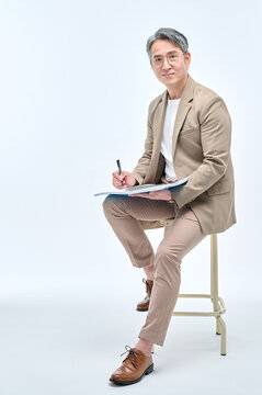 A middle-aged male teacher in a suit and glasses is sitting in a chair, holding writing tools and notes, with various expressions and poses.