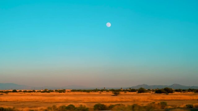 View of the full moon clearly showing in the dawn sky over the desert as seen from a moving car