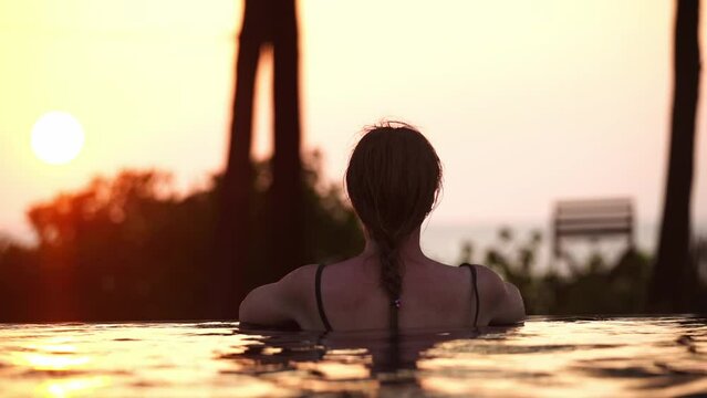 A girl looks at the sunset from a pool by the sea