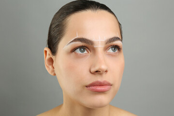 Eyebrow correction. Young woman with markings on face against grey background