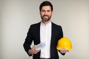 Architect with draft and hard hat on gray background