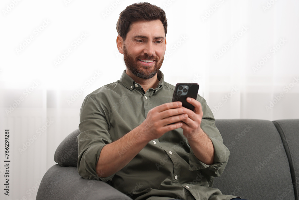 Poster smiling man using smartphone on sofa at home