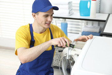 Smiling plumber with screwdriver repairing washing machine in bathroom