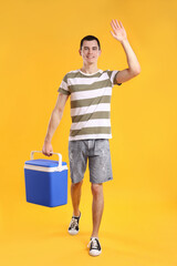 Man with blue cool box walking and greeting someone on orange background