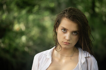 Portrait of a young brunette with wet hair posing in a white wet  shirt.  Horizontally. 