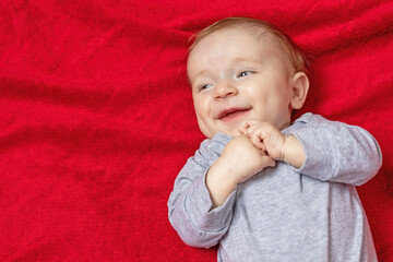 Top view of laughing baby boy lying on red blanket. The child looks at the free space ready for your use.