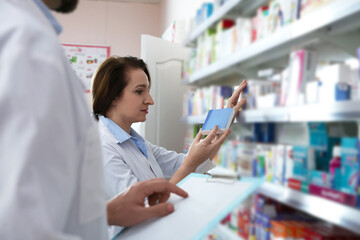 Professional pharmacists near shelves with merchandise in modern drugstore