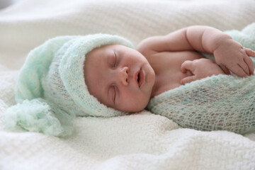 Cute newborn baby in warm hat sleeping on white plaid