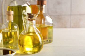Vegetable fats. Different oils in glass bottles on white wooden table, closeup. Space for text