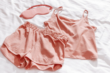 Pink woman pajamas and sleep eye mask on white bed sheet. Top view summer pyjama for sleeping....