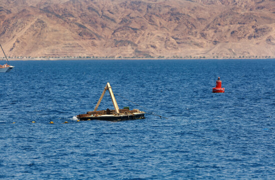 A serene seascape with a buoyant structure and a red buoy floating on the calm blue sea. In the background, majestic mountains stand tall, Red sea, Israel. Red navigation buoys and mountain backdrop
