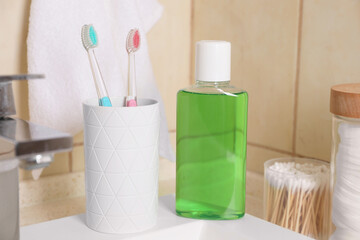 Fresh mouthwash in bottle and holder with toothbrushes on sink in bathroom, closeup