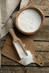 Fototapeta na wymiar Baking powder in bowl and scoop on wooden table, flat lay