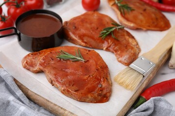 Raw marinated meat, rosemary and basting brush on table, closeup