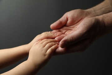 Father and child holding hands on dark grey background, closeup