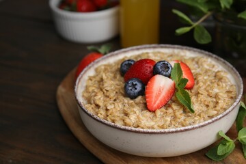 Tasty oatmeal with strawberries and blueberries in bowl on wooden table. Space for text