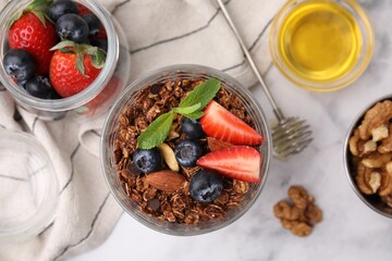 Tasty granola with berries, nuts, honey and whisk on white marble table, flat lay