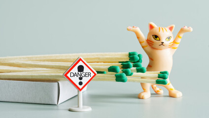 Funny ginger toy kitten with raised paws next to open matchbox and Danger warning sign. Concept of teaching children fire safety rules. Light background. Selective focus - obrazy, fototapety, plakaty