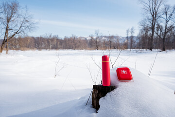 Pink thermos and first aid kit lying on the snow