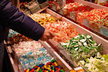 A sweet tooth  adult man make a choice buying colorful sweet candy in candy shop.  Concept of over consume sugar can lead to health issues.  