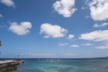 Seascape. Dock of the village of Arrieta, group of boats anchored nearby. Mountains in the background. Turquoise Atlantic Ocean. Big white clouds. Village of Arrieta. Lanzarote, Canary Islands, Spain