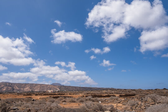 Deserted landscape on the outskirts of the village of Arrieta. Dry bushes, red earth and mountains in the background. Large white clouds. Village of Arrieta. Lanzarote, Canary Islands, Spain