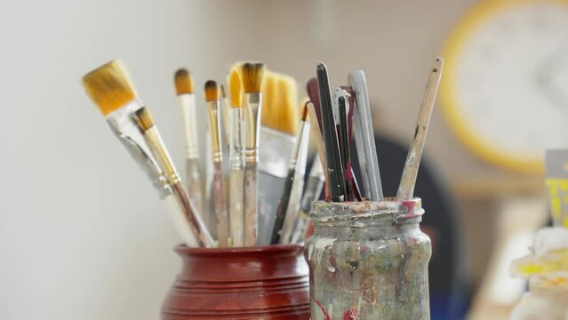 Painter returns brush in glass. Art concept. Female artist hand puts brush for painting into glass. Unrecognizable young artist choosing brushes. Close-up in 4K, UHD
