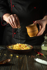 The chef salts pasta in a plate on the kitchen table. Low key concept of preparing a delicious lunch in a saloon. Advertising space