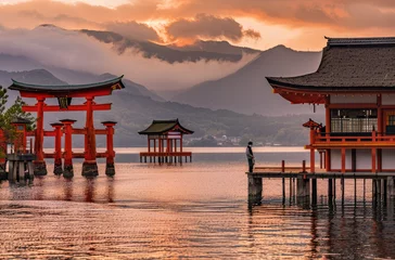 Foto op Plexiglas A beautiful landscape photo of the Torii gate at its base on an island surrounded by water with mountains behind it and an orange sky © Kien