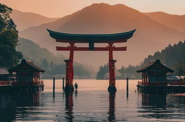 Foto auf Acrylglas A beautiful landscape photo of the Torii gate at its base on an island surrounded by water with mountains behind it and an orange sky © Kien