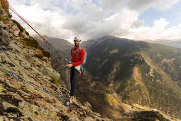 A man in a red jacket is standing on a rock face with a rope attached to him. He is wearing a helmet and he is preparing for a climb. Concept of adventure and excitement