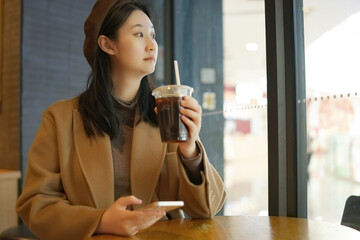 Young Woman Savoring Coffee and Browsing Phone at Cafe