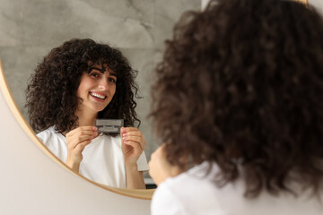 Young woman holding teeth whitening strips indoors