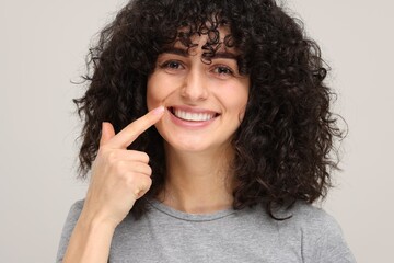 Young woman showing her teeth with whitening strip on light grey background