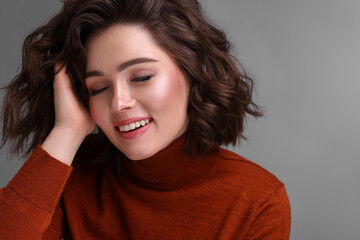 Fototapeta premium Beautiful young woman with wavy hairstyle on grey background