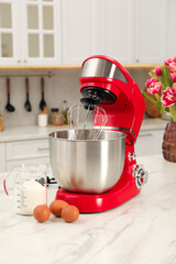 Modern red stand mixer, eggs and container with flour on white marble table in kitchen