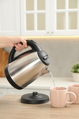 Woman pouring hot water from electric kettle into cup in kitchen, closeup - obrazy, fototapety, plakaty