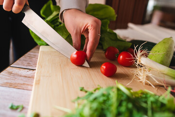 A close up of girl's or woman's hands peeling and cutting vegetables with knife making salad	